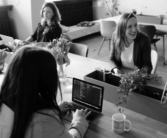 female co-workers using laptops at their desk, one of them is laughing